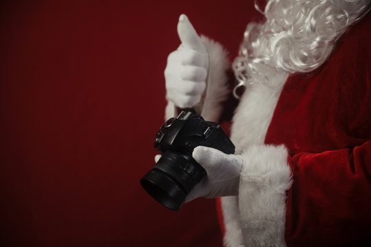 Santa Claus using DSLR camera taking images showing thumb up. Happy Christmas Evening and New Year celebration background. Fun loving creative costume time.