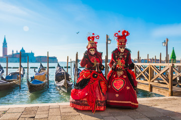 Couple wearing venitian carnival mask in front of gondolas in Grand Canal during Venice carnival in...