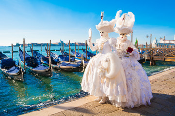 Couple wearing venitian carnival mask in front of gondolas in Grand Canal during Venice carnival in...