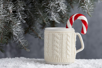 Obraz na płótnie Canvas Knitted winter cup of hot chocolate with candy cane on snowy table under christmas tree