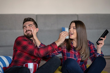 Couple fighting for remote control while watching TV at home