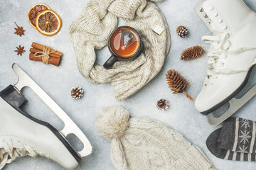 Fototapeta na wymiar Winter vacation concept. Skates warm clothes, Cup of hot tea with fragrant spices on grey background.