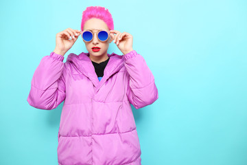 Fashion portrait of young hipster woman in lilac down jacket. Short pink hair, sunglasses, red lips, turquoise background