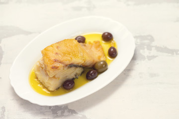 fried cod fish with olives and olive oil on white dish