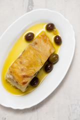 fried cod fish with olives and olive oil on white dish