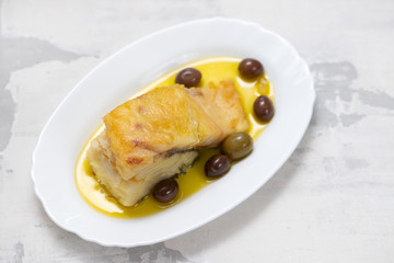 fried cod fish with olives and olive oil on white dish