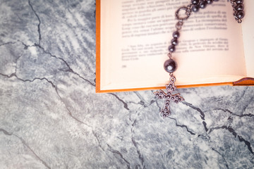 Black rosary and cross on the Bible on a gray surface. Religion at school.