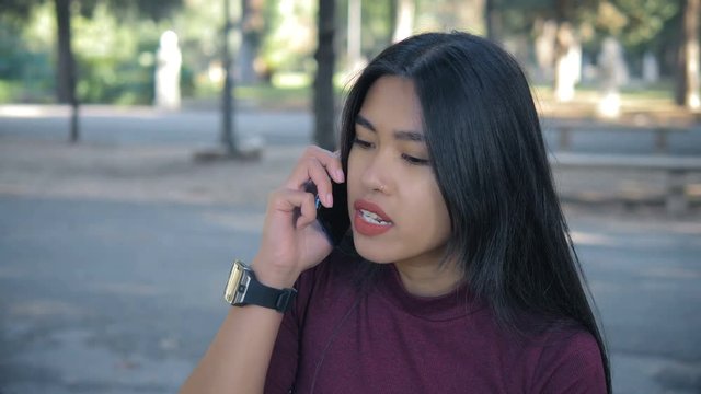Angry asian  young woman talking by phone in the park. anger, discussion, argue