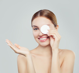 Attractive woman cleaning her face with a cotton pad on white background. Cheerful young woman...
