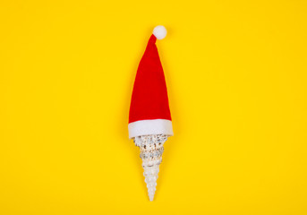 Seashell wearing a Santa hat on the bright yellow background as the tropical Christmas concept (top view, minimal style)