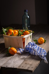 Basket of tangerines on a rustic kitchen table with a white and blue check cloth and a bottle