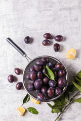 Ripe juicy plums on a colander, on old white wooden table.