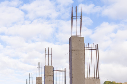 Baustelle mit gegossenen Betonst&uuml;tzen mit Armierungseisen vor blauem Himmel mit Wolken