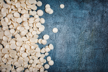 Top view of white chocolate drops or morsels on blue concrete background