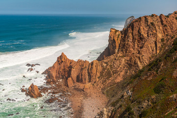 Fototapeta na wymiar Stunning landscape of cliffs rising from the turquoise waters of the Ocean on a sunny summer day. Cape Roca (Cabo da Roca), the most western point of Europe in Sintra, Portugal.
