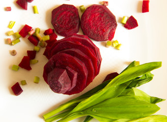 Sliced beetroot with green leaves of wild garlic on white background