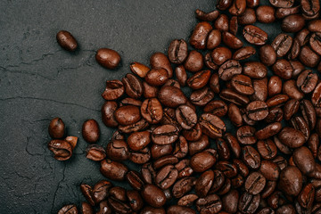 Roasted brown coffee beans on the black concrete stone background. Flatlay style, messy pattern.