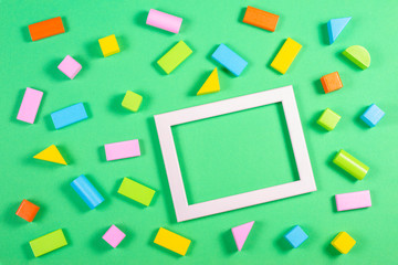 Fototapeta na wymiar Toys background with empty photo image frame and colorful wooden cubes pattern on green color background