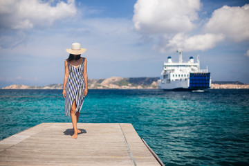 Beautiful young woman in hat walking on wooden pier on Sardinia beach