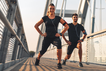 Young couple in black sports outfit doing morning workout outdoors. Young man and woman stretching...