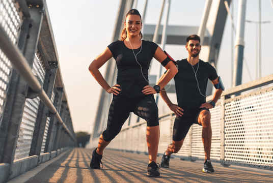 Young couple in black sports outfit doing morning workout outdoors. Young man and woman stretching they muscle before running on bridge.	