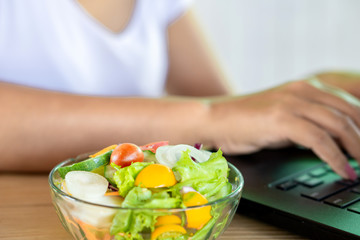 Fototapeta na wymiar salad bowl on desk with woman working on laptop 