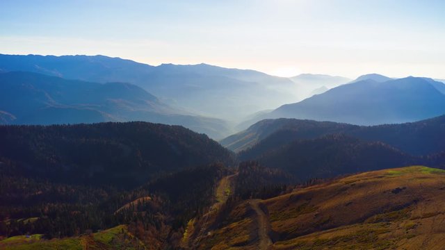 Beautiful aerial view to the evening mountains in Sochi Roza Hutor. Picturesque motion timelapse of autumn valley with the sun behind the peaks and hazy sunshine. 8K ultra high definition footage.