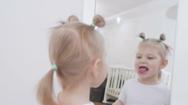 Cute little girl sitting in front of a mirror is painting lips with hygienic lipstick