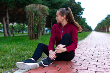 A young, fitness girl in sneakers and sportswear was injured while jogging and sports training. Leg injury and muscle strain, and ankle sprain accident during sports exercise.