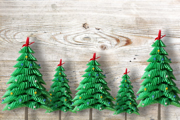 Five Christmas trees from green folded paper or origami on wooden background