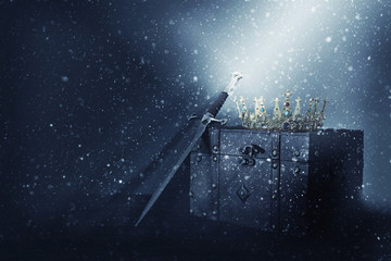 mysterious and magical image of old crown, wooden chest and sword over gothic black background....