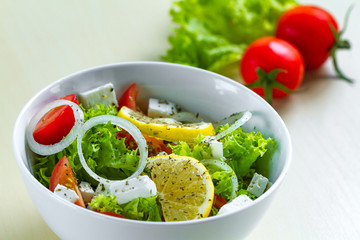 Fresh, healthy vegetable salad with lettuce, cherry tomatoes, onion, feta cheese, lemon, sprinkled with spices in a plate. Proper nutrition and right food. Diet