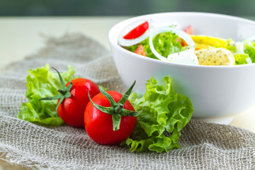 Fresh, healthy vegetable salad with lettuce, cherry tomatoes, onion, feta cheese, lemon, sprinkled with spices in a plate. Proper nutrition and right food. Diet