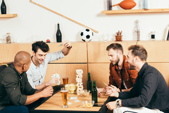 multicultural men playing cards while spending time together in cafe