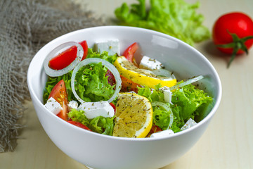 Fresh, healthy vegetable salad with lettuce, cherry tomatoes, onion, feta cheese, lemon, sprinkled with spices in a plate. Proper nutrition and right food. Diet