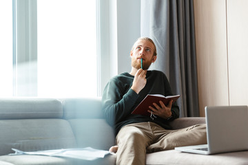 Concentrated young bearded man sitting in home writing notes.