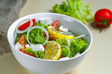 Fresh, healthy vegetable salad with lettuce, cherry tomatoes, onion, feta cheese, lemon, sprinkled with spices in a plate. Proper nutrition and right food. Diet