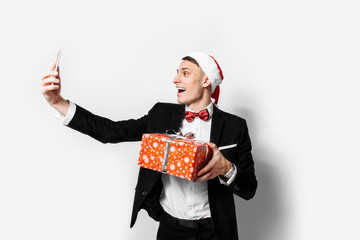 Shocked guy in a suit and a santa hat, in his hands - a Christmas gift, he takes pictures of...