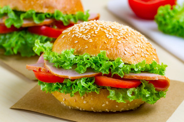 Appetizing sesame buns with fresh lettuce, tomato and ham for snack. Homemade sandwiches