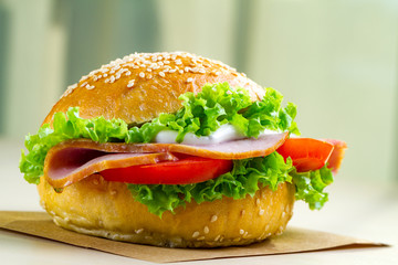 Appetizing sesame bun with fresh lettuce, tomato and ham for snack close up. Homemade sandwiches