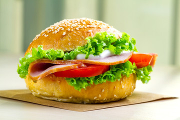 Appetizing sesame bun with fresh lettuce, tomato and ham for snack close up. Homemade sandwiches