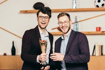 portrait of smiling businessmen with champions goblet in cafe