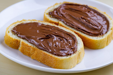 Pieces of long loaf with chocolate, nut paste on a plate. Nut chocolate cream sandwich with nut butter on a breakfast