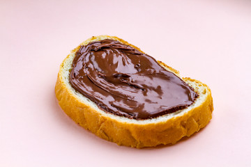 Piece of loaf with spread chocolate paste on a pink background. Sweet, nut butter with fresh bread for breakfast. Chocolate sandwich