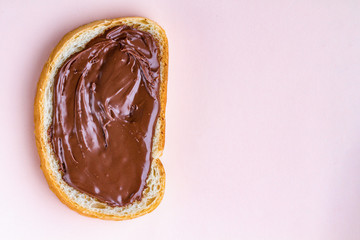Piece of loaf with spread chocolate paste on a pink background. Sweet, nut butter with fresh bread for breakfast. Chocolate sandwich. Copy space