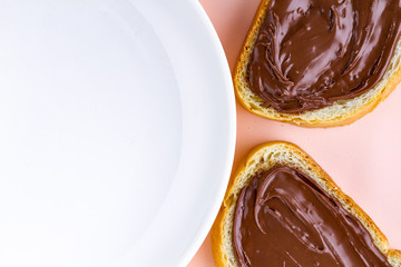 Pieces of loaf with chocolate paste and a plate on a pink background. Chocolate sandwiches with nut paste on a breakfast. Top view. Copy space