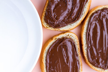 Pieces of loaf with chocolate paste and a plate on a pink background. Chocolate sandwiches with nut paste on a breakfast. Top view. Copy space