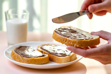 Spread chocolate paste on freshly baked bread. Chocolate sandwiches with nut, sweet paste and a glass of milk for a breakfast.