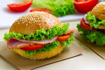 Appetizing sesame buns with fresh lettuce, tomato and ham for snack. Homemade sandwiches