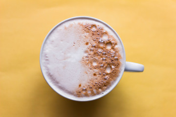 Cup of cappuccino coffee on yellow background, top view